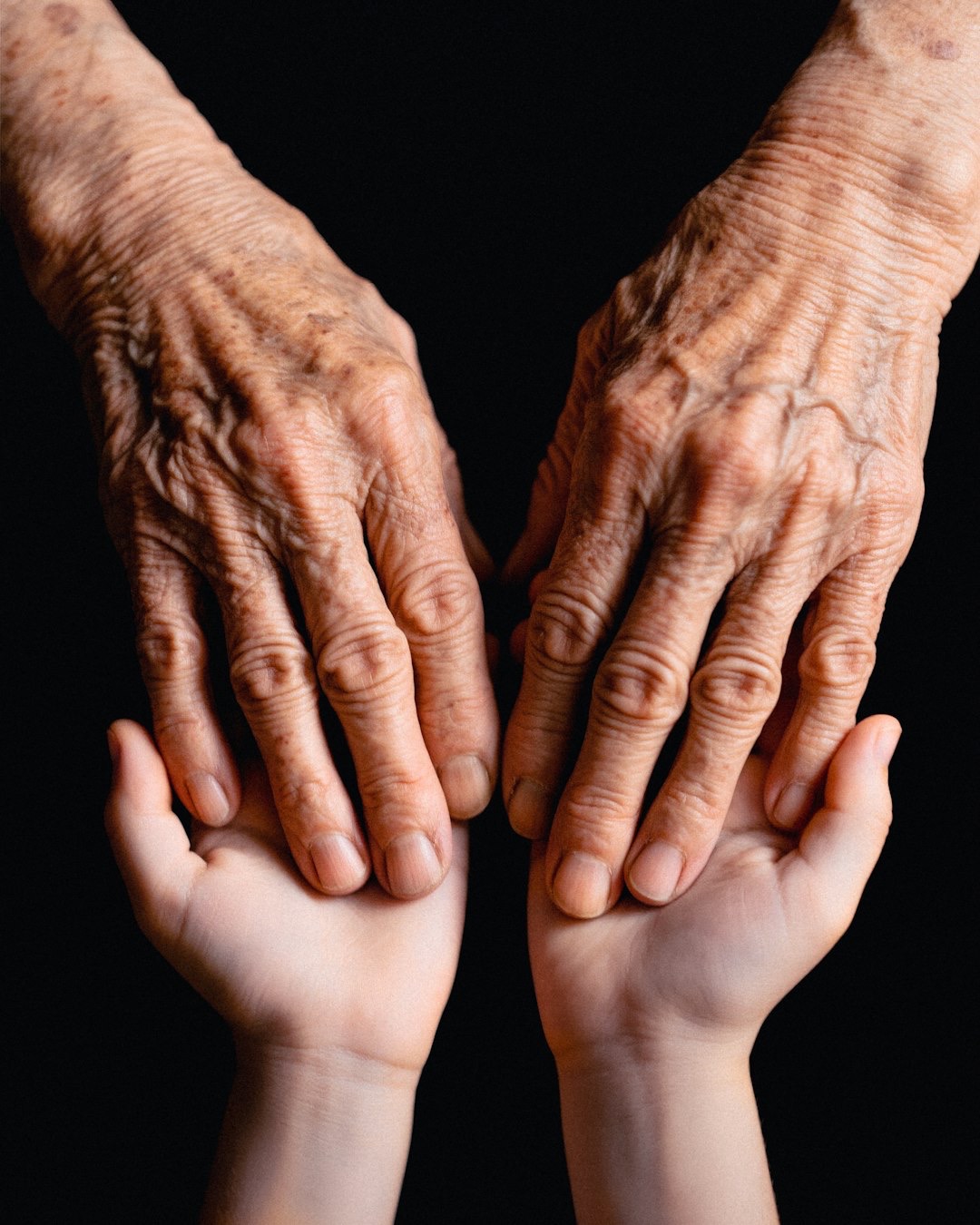 Older person placing their wrinkled hands on younger hands.